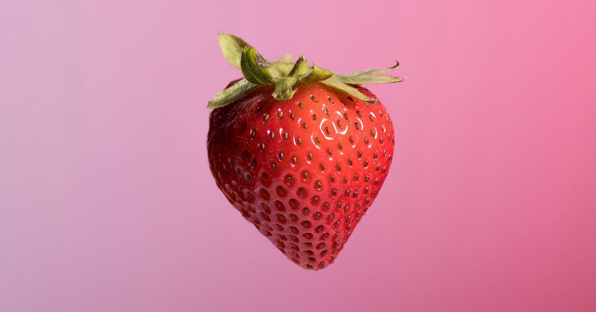 A single strawberry is pictured against a pink ombre background