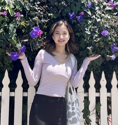 Calynn Wang smiling in front of a fence and flowers