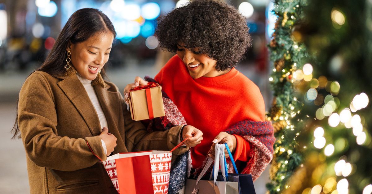 Two female friends are enjoying the Christmas spirit by giving each other presents in a beautifully decorated city street