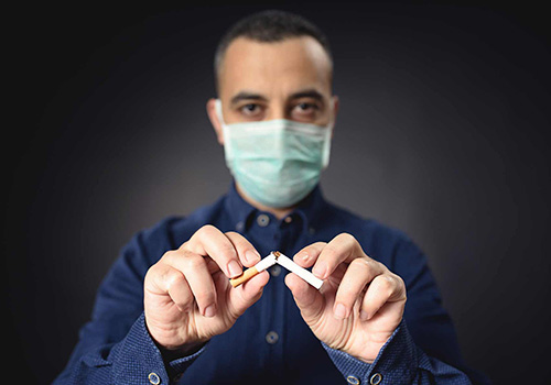 Man breaking a cigarette in half while wearing a face mask